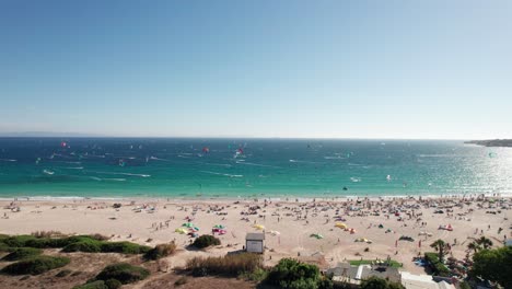 approach-aerial-view-of-kitesurfers-practicing-and-having-fun-at-Tarifa-Beach,-Cadiz,-spain