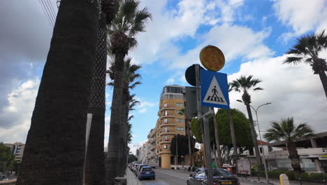 Close-up-view-of-a-pedestrian-crossing-sign-and-palm-trees-along-a-street-in-Nicosia,-Cyprus