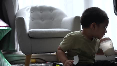 South-Asian-18-Month-Old-Toddler-Boy-Drinking-Milk-While-Sitting-On-The-Floor-At-Home-And-Being-Playful