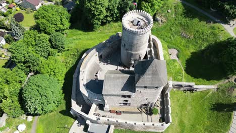 Medieval-castle-with-a-tower,-walls,-and-courtyard-during-a-beautiful-summer-day-surrounded-by-lush-greenery,-grass,-and-trees