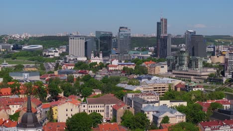 Drone-Flies-Away-from-Modern-Vilnius-Skyscraper-Buildings,-Reveals-Cathedral,-Bell-Tower
