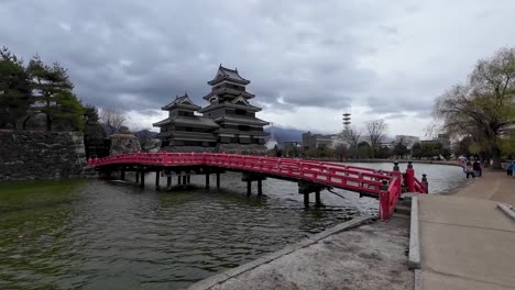 Japanische-Burg-Mit-Einer-Roten-Brücke,-Die-Zur-Burg-Führt,-Und-Wasser-Davor-An-Einem-Bewölkten-Tag