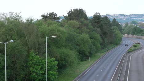 Lone-Car-on-Dual-Carriageway-Road-at-Sunrise-with-Trees-and-Street-Lights