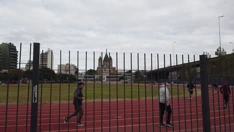Menschen-Laufen-Auf-Der-Laufstrecke-Parque-Chacabuco-In-Buenos-Aires-Mit-Kirchlichem-Hintergrund