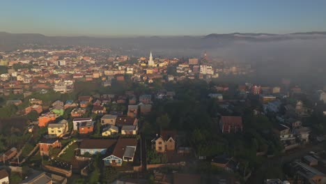 Vista-Aérea-De-Antsirabe,-La-Tercera-Ciudad-Más-Grande-De-Madagascar-Con-Casas-E-Iglesias-En-Una-Mañana-Soleada-Con-Niebla