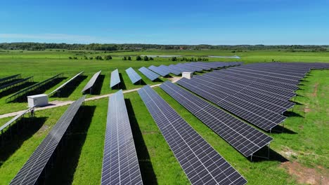 A-large-solar-panel-field-in-a-lush-green-landscape-under-a-clear-blue-sky,-aerial-view