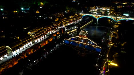 Aerial-flying-over-illuminated-Phoenix-Ancient-Town-and-Snow-Bridge,-China