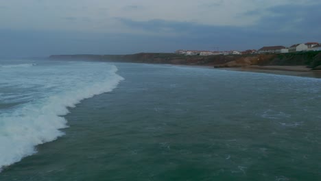 Toma-Aérea-De-Un-Dron-Siguiendo-Una-Ola-Rompiendo-Al-Atardecer-En-La-Playa-De-Baleal,-Portugal