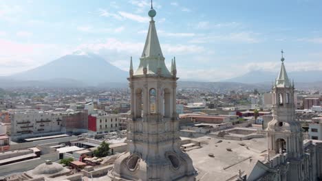 Enjoy-a-stunning-close-up-pan-of-one-of-the-towers-of-Arequipa-Cathedral,-with-the-majestic-Misti-volcano-and-the-imposing-Chachani-in-the-background,-on-a-peaceful-day-surrounded-by-clouds