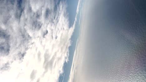 Filmische-Vertikale-Luftaufnahme-Des-Meeres-Mit-Vielen-Reflexionen-Zwischen-Den-Wolken-Und-Dem-Himmel
