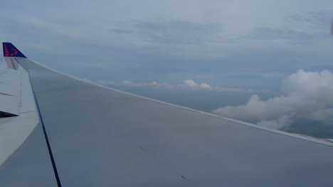 Flügel-Eines-Flugzeugs-Vom-Fenster-Aus-Gesehen,-Das-Hoch-über-Den-Wolken-Fliegt,-Mit-Einem-Klaren-Himmel-Im-Hintergrund