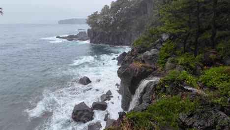 Espectacular-Línea-Costera-Con-Fuertes-Olas-Rompiendo-A-Lo-Largo-De-Los-Acantilados-Con-Vista-Al-Mar-Y-Al-Océano-Desde-El-Lado-Del-Bosque-Y-Una-Cascada-Proveniente-Del-Río-Que-Cae-Al-Océano