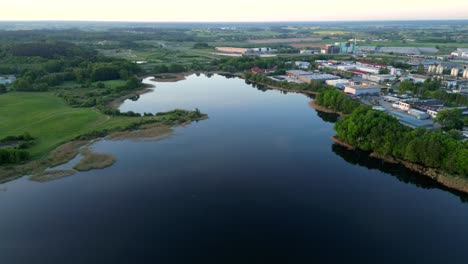 Panorama-Al-Amanecer,-Vista-Por-Drones-De-Los-Edificios-Del-Distrito-Industrial-De-La-Ciudad-Ubicados-Más-Allá-De-Las-Orillas-Del-Lago