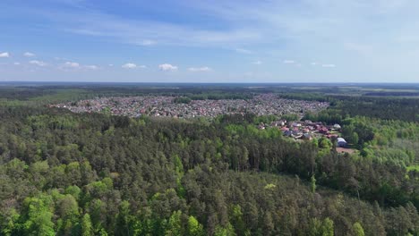 A-small-town-surrounded-by-dense-green-forest-and-river-on-a-sunny-day,-aerial-view