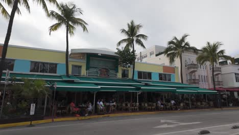 Lebendige-Straßenszene-In-Miami-Beach-Mit-Farbenfrohen-Gebäuden-Und-Palmen-An-Einem-Bewölkten-Tag