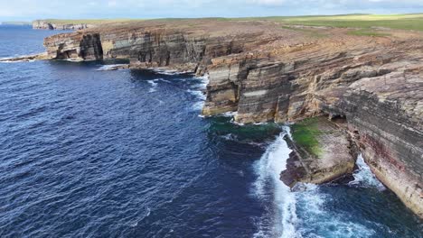 Aerial-View-of-Ocean-Waves-Crashing-Under-Cliffs-on-Coastline-of-Scotland-UK,-Yesnaby-Vista-Point-of-Sunny-Day