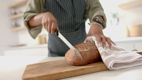 African-American-young-woman-wearing-apron-is-slicing-bread-on-wooden-board