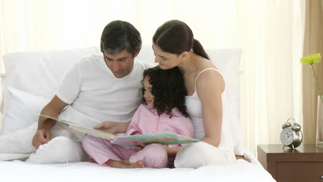 Parents-reading-a-book-on-bed-with-their-daughter-