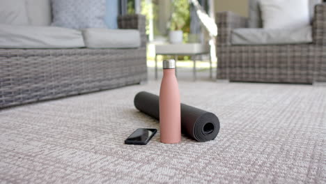 A-smartphone-and-water-bottle-are-resting-next-to-a-rolled-up-yoga-mat
