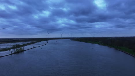 Vuela-Sobre-El-Río-Con-Turbinas-Eólicas-Al-Fondo-Durante-La-Puesta-De-Sol-Cerca-De-Barendrecht,-Países-Bajos