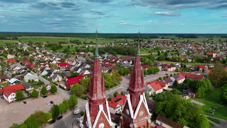 A-church-with-twin-towers-in-a-colorful-lithuanian-village-during-a-sunny-day,-aerial-view