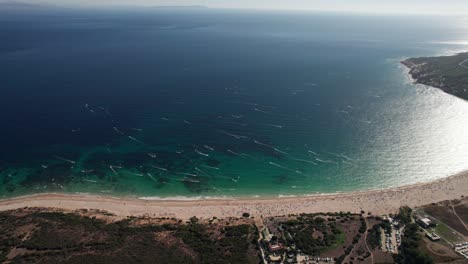 Panorama-Luftaufnahme-Von-Vielen-Kitesurfern,-Die-An-Einem-Sonnigen-Tag-Am-Strand-Von-Tarifa,-Cadiz,-Spanien-Spaß-Haben