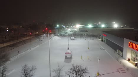 Snowfall-at-Canadian-Tire-Parking-Lot-with-an-Aerial-Drone-Overhead-Panning-at-Floodlight,-Montréal,-Québec,-Canada