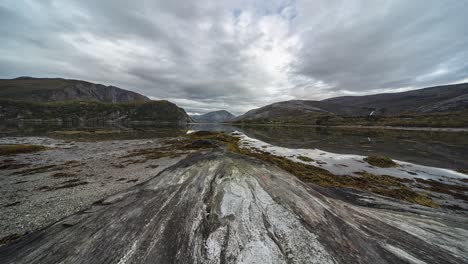 Heavy-clouds-fly-above-the-rocky-shores-and-sandy-bottom-of-the-fjord-exposed-by-the-low-tide-in-a-timelapse-video