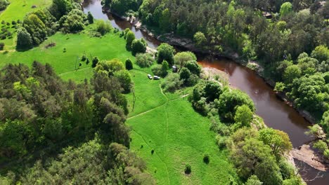 A-lush-green-forest-landscape-with-a-winding-river-on-a-sunny-day,-aerial-view