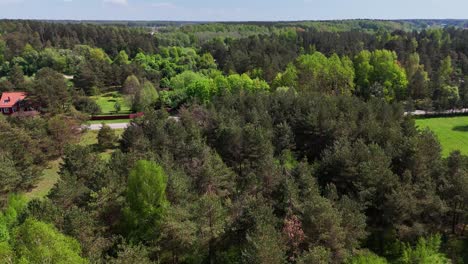 A-dense-forest-with-a-small-town-in-the-distance,-lithuania,-aerial-view