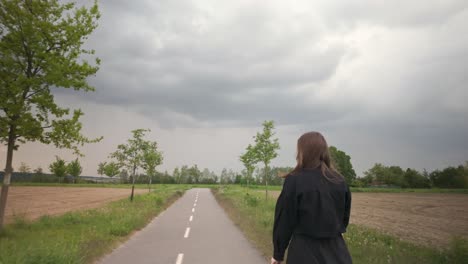 Girl-in-a-long-black-dress-walks-along-a-path-lined-with-trees