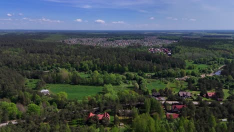 Un-Pequeño-Pueblo-Rodeado-De-Un-Vasto-Bosque-Verde-Y-Un-Cielo-Azul,-Vista-Aérea