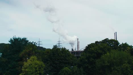 Weite-Kinoaufnahme-Eines-Kraftwerks,-Aufsteigender-Rauch,-Aufnahme-Mit-Bäumen-Im-Vordergrund