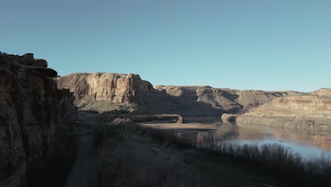 Paisaje-Desolado-En-Utah,-EE.UU.,-Con-Un-Camino-Sinuoso-Cerca-De-Un-Río-Y-Majestuosas-Colinas-Al-Fondo