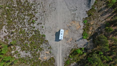 Birds-eye-drone-shot-following-a-camper-van-driving-in-a-sand-pit,-sunny-day