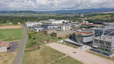 Drone-flying-up-to-an-elderly-care-home-surrounded-by-offices-and-industrial-building-with-a-beautiful-Swiss-landscape-in-the-background
