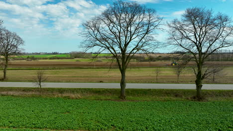 Una-Vista-Desde-El-Borde-De-Un-Campo-Con-Dos-árboles-Desnudos-Que-Enmarcan-La-Escena