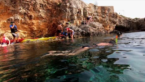A-group-of-people-relax,-swim,-and-snorkel-in-a-beautiful,-hidden-little-rocky-bay-on-the-Mediterranean-island-of-Comino,-Malta