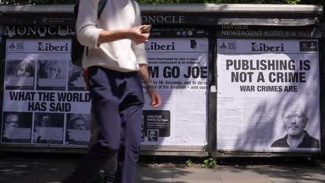 En-Cámara-Lenta,-La-Gente-Pasa-Junto-A-Carteles-En-Un-Quiosco-Que-Muestran-Portadas-De-Periódicos-Con-Los-Titulares-&quot;lo-Que-El-Mundo-Ha-Dicho&quot;,-&quot;déjalo-Ir,-Joe&quot;-Y-&quot;publicar-No-Es-Un-Crimen,-Los-Crímenes-De-Guerra-Sí-Lo-Son&quot;.