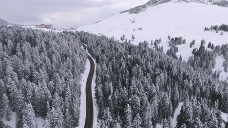 Luftaufnahme-Einer-Bergstraße,-Die-Von-Verschneiten-Wäldern-Umgeben-Ist-Und-Im-Winter-Auf-Einer-Berghütte-Endet