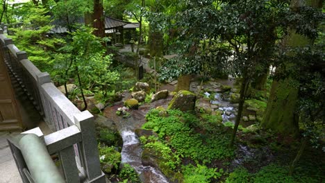 Slow-motion-rotating-shot-of-temple-in-lush-green-forest-with-small-waterfall