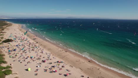 aerial-video-of-kitesurfers-practicing-and-people-enjoying-the-beach-during-sunny-day-at-Tarifa-Beach,-Cadiz,-spain