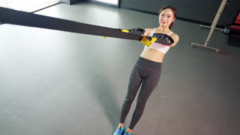 Athletic-muscular-fitness-woman-showing-suspension-training,-performing-pull-ups-exercise-with-trx-straps-at-gym