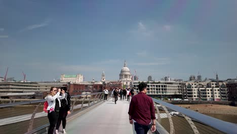 Walking-across-the-Millennium-Bridge-in-London,-England,-amid-pleasant-weather,-as-people-stroll-along-the-bridge,-encapsulating-a-leisurely-urban-experience