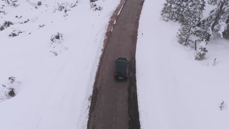 Rising-drone-shot-of-black-car-on-mountain-road-during-peaceful-winter-day-in-Italy