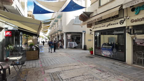 A-charming-pedestrian-street-in-Nicosia,-Cyprus,-lined-with-shops-and-cafes,-with-colorful-canopies-providing-shade,-captured-in-slow-motion