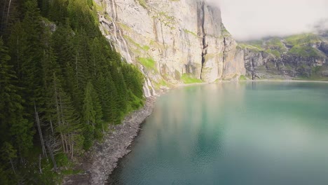 Aerial-flight-towards-a-beautiful-big-waterfall-on-a-mountain-Landscape,-Drone-Flying-Over-a-Blue-Lake---Oeschinen-Lake,-Switzerland