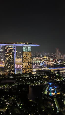Rotating-nighttime-aerial-of-the-Marina-Bay-Sands-Resort-and-surrounding-area-in-Singapore,-vertical-video