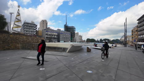 A-modern-plaza-in-Nicosia,-Cyprus,-with-people-walking-and-cycling,-set-against-a-backdrop-of-high-rise-buildings-and-a-clear-sky,-captured-in-slow-motion