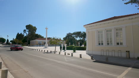 A-wide-street-view-of-a-public-square-in-Pafos,-Cyprus,-with-historic-buildings-and-columns-under-a-clear-blue-sky